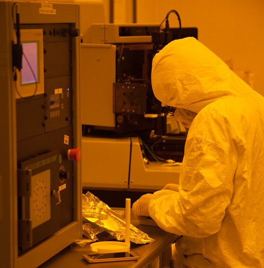 Technician in a clean room wearing protective clothing using a piece of electronics machinery